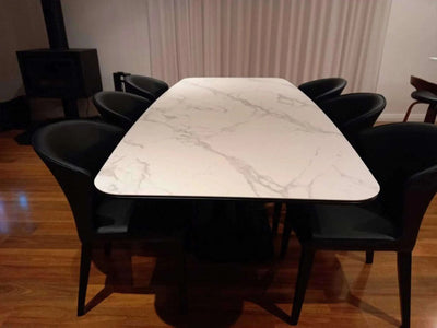 Spanish Marble Ceramic Dining Table with white marble finish and black chairs in dining room setting.