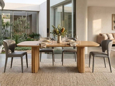 Ashford Dining Table with a natural honey-toned wood top and paired cylindrical pillar legs, displaying visible grain and rounded edges.