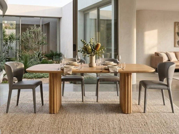 Ashford Dining Table with a natural honey-toned wood top and paired cylindrical pillar legs, displaying visible grain and rounded edges.