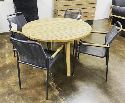 Atoll Outdoor Teak Round Dining Table in an outdoor setting with black mesh chairs.