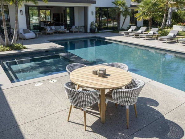 Outdoor teak round dining table with four woven chairs by poolside in modern patio setting