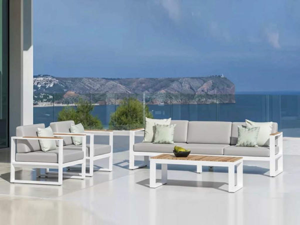 Belvedere 3 seater outdoor sofa with aluminum frame, teak arm trims, and grey Sunbrella cushions on a patio overlooking the sea.