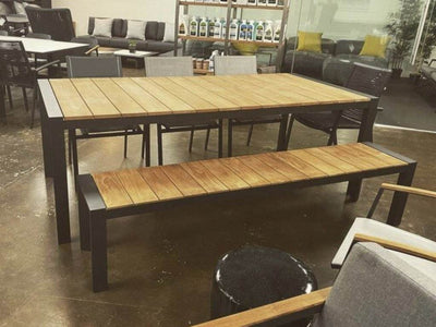 Cebu Outdoor Teak Dining Table with aluminum base, shown in charcoal, surrounded by outdoor seating.