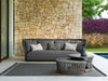 Cliff Outdoor 3 Seater Woven Rope Sofa in dark grey with geometric cushions on patio by stone wall