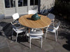 Coco Outdoor Dining Chair with teak armrest trims around wooden table on patio.