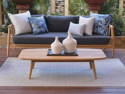 Finley Outdoor Teak Coffee Table in elegant patio setting with cushions and decor.