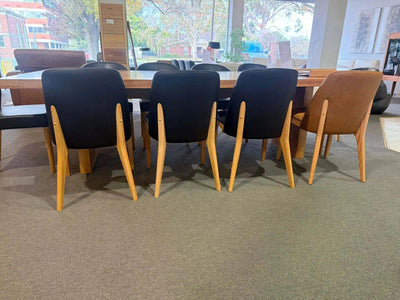 Kai Leather Dining Chair in black and tan with timber legs around a dining table in a modern interior setting.