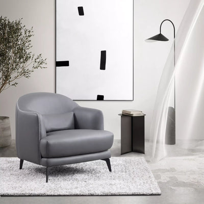 Kartik Leather Armchair in gray with sleek metal legs, rounded back, and lumbar cushion, set in modern interior.