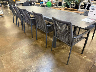Milan Outdoor Rope Chair with woven design and aluminum frame in charcoal color, set around a large outdoor dining table.