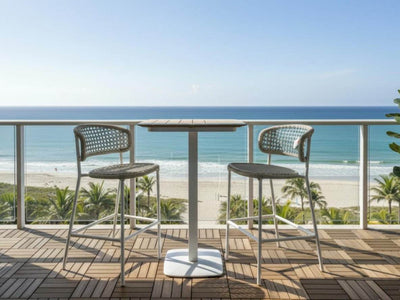 Moorea outdoor teak bar table with white aluminum frame and two woven chairs on balcony overlooking beach