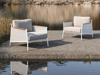 Nine Degrees Outdoor Lounge - 1 Seater Sofa with teak armrests and white aluminum frame by a water edge.