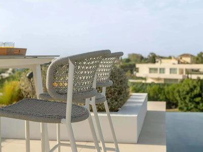Butterfly Outdoor Bar Chair with elegant woven backrest, durable aluminum frame, and Italian polyethylene rope in outdoor setting.