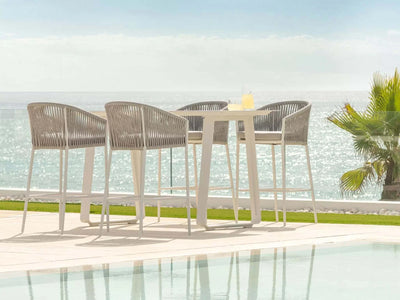 Jiselle Outdoor Bar Chair by the pool with ocean view, features white frame with grey rope and Sunbrella cushions.
