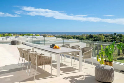 Jiselle Outdoor Rope Dining Chair on a terrace; elegant design with white frame, grey Italian rope weaving, and Sunbrella cushions.