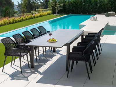Livorno Outdoor Ceramic Extendable Dining Table by poolside with black chairs.