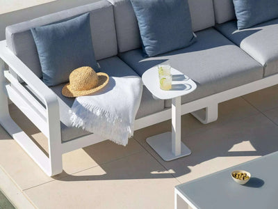 Tucino Outdoor Side Table in white finish next to a modern outdoor sofa, with a glass of lemonade and a hat.