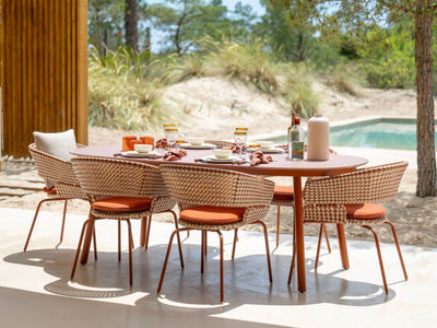 Palma rust outdoor dining table and wicker dining chairs beside a pool