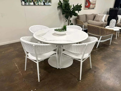Pisa Outdoor Ceramic Round Dining Table with white chairs and decor, featuring a sleek ceramic top and sturdy aluminum frame.