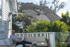 Retreat Wall-Mounted Outdoor Umbrella in grey providing shade over a man sitting on a beige outdoor sofa on a balcony