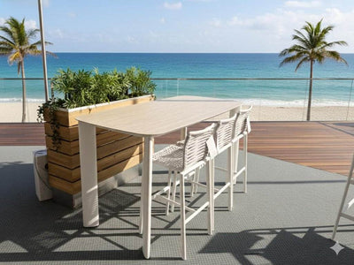 Sierra Outdoor Bar Table with 6mm ceramic travertine top and white powder-coated aluminum frame on beach deck
